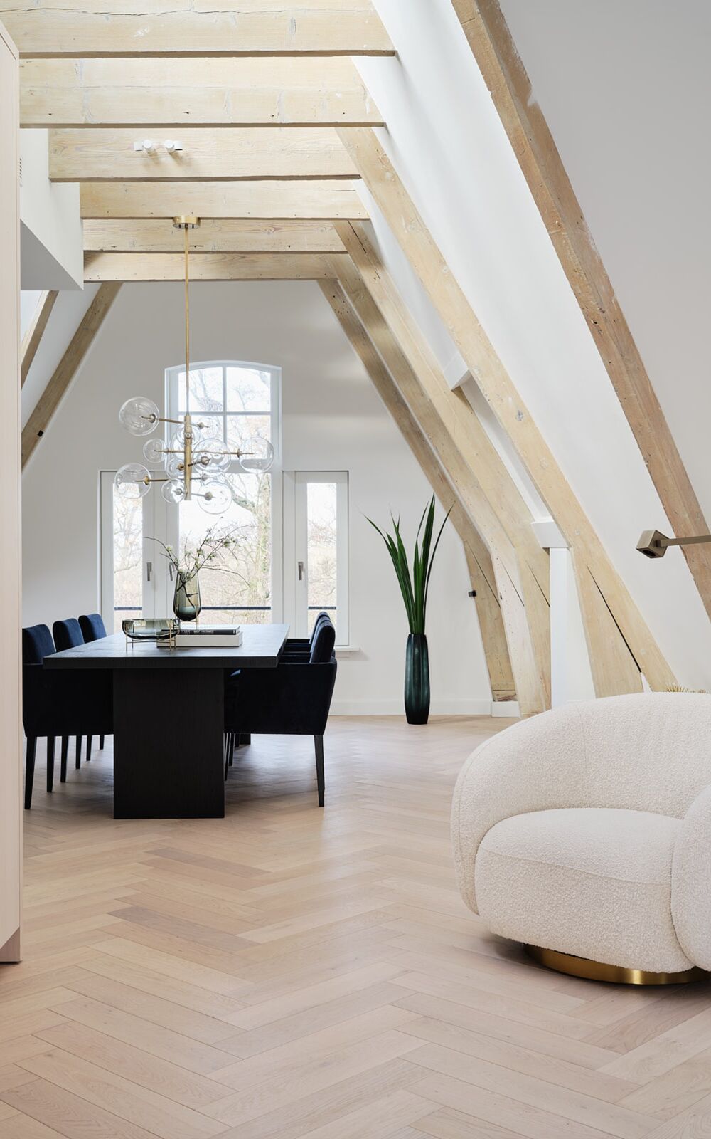 Eettafel onder houten spanten bij een hoog raam